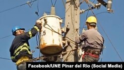 Dos trabajadores de la UNE de Pinar del Río están trabajando en un poste.